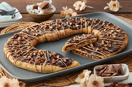 Turtle Kringle on a white plate with chocolate chunks drizzled with caramel. 