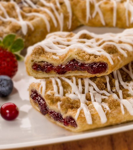 Berry Crumble Kringle on white plate with mixed berries. 