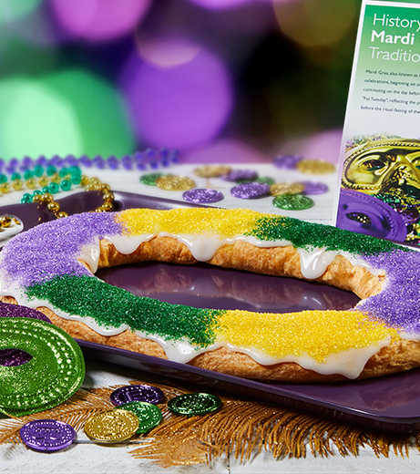 Mardi Gras Kringle on purple tray with history card, bead necklaces, mask, coins in mardi gras colors.