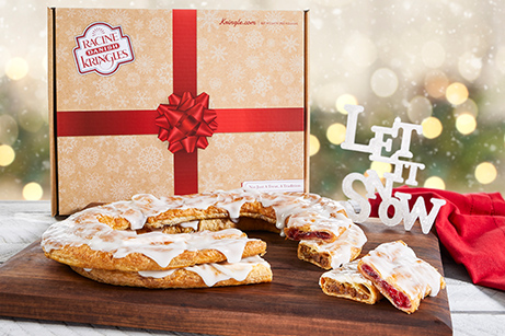 Holiday Box with red bow in artwork with pecan and raspberry Kringle on white plate surrounded by holiday decorations. 