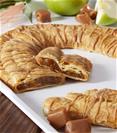 Caramel Apple Kringle on white tray surrounded by sliced apple, cubed caramel pieces and grey napkin.