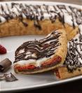 Chocolate Strawberry Kringle on a white plate surrounded by a bowl of strawberries and chucks of chocolate. 