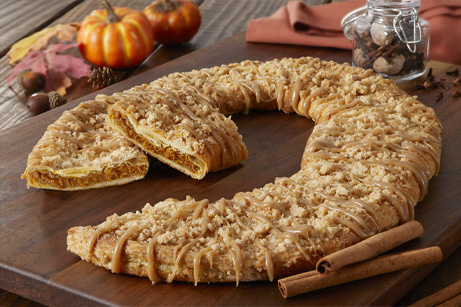 Pumpkin Spice Kringle on wood board with pumpkins, spice and cinnamon sticks on the side.