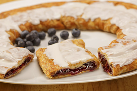 Blueberry Kringle on white plate with scattered blueberries. 
