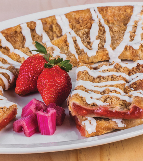Strawberry Rhubarb Kringle on a white plate with sliced strawberries and rhubarb.