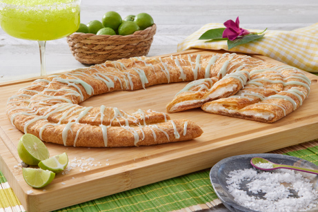 Margarita Kringle on a wooden cutting board surrounded by limes and salt.