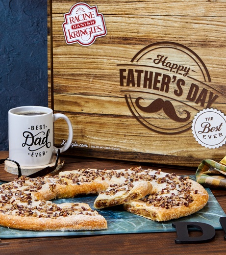 Wood grained patterned box with bourbon pecan Kringle in front "best dad" coffee mug, eye glasses, and bow tie. 