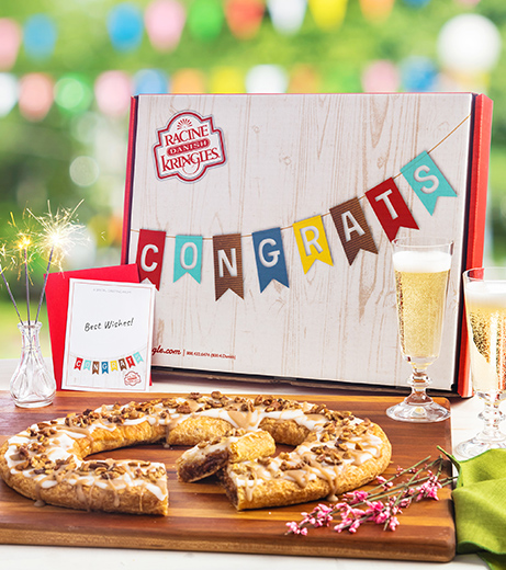Light wood grain box with Congrats banner with two champagne flutes, sparkers and Kringle on wood board. 