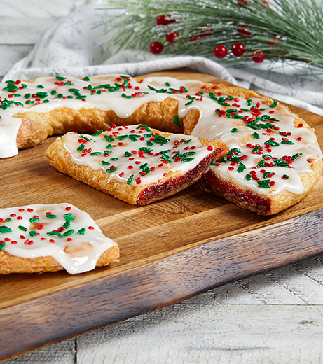 Santa's Cinnaberry Kringle on wood board with bowl of cranberries, cinnamon sticks and festive pine branch. 