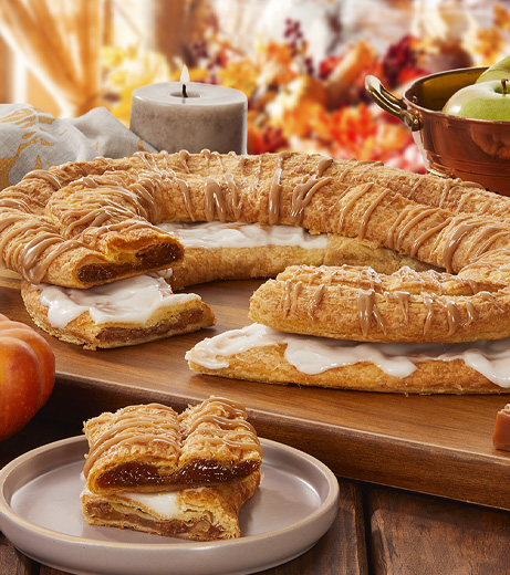 Pumpkin Caramel and Apple Cinnamon Kringle with slices cut out on separate plate surrounded by pumpkin, caramel cubes, apples and fall decorations. 