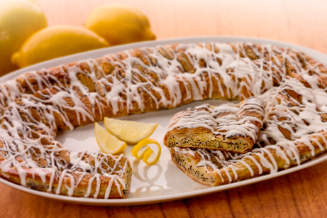 Lemon poppyseed kringle with a drizzle of icing with a close up shot and a wide angle view of the kringle on a platter