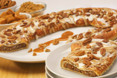 Praline Pecan Kringle on white plate with bowls of brown sugar, pecans, and caramel cubes. 