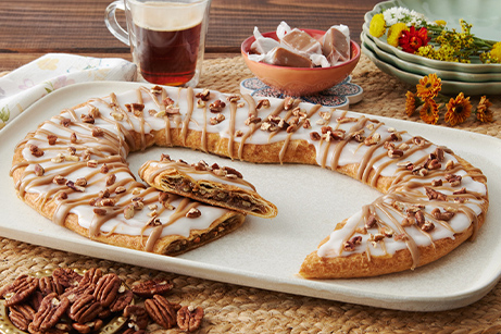 Praline Pecan Kringle on white plate with bowls of brown sugar, pecans, and caramel cubes. 