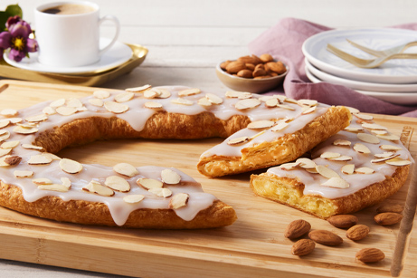Almond Kringle sitting on a white plate with a few almonds next to the Kringle. 