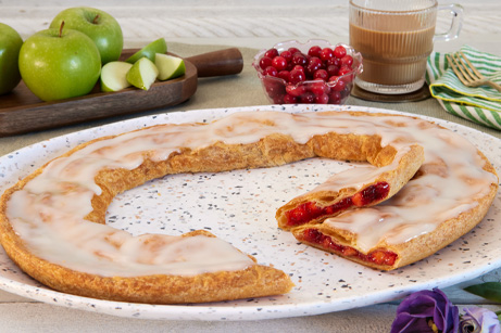 Cranberry Apple Kringle on white plate with apple slices and scattering of cranberries. 