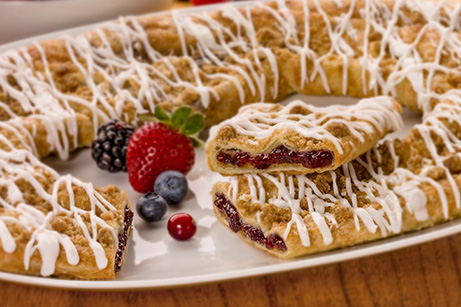 Berry Crumble Kringle on white plate with mixed berries.