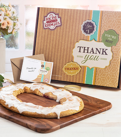 Tan designed box with "thank you" badges with a Kringle on a wood board next to case of flowers. 