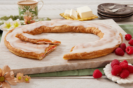 Raspberry Cheesecake Kringle on white plate, slice on smaller plate surrounded by raspberries.