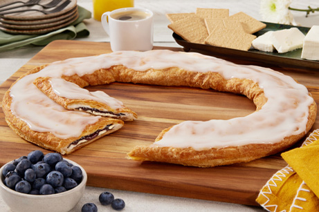 Blueberry Cheesecake Kringle on a white plate surrounded by blueberries. 
