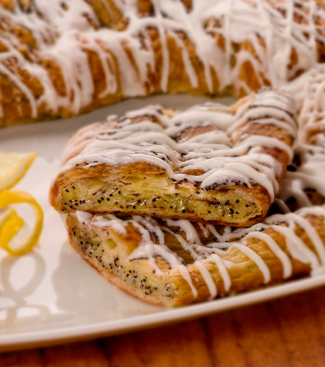 Lemon poppyseed kringle with a drizzle of icing with a close up shot and a wide angle view of the kringle on a platter