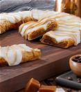 Caramel Macchiato Kringle on wood board surrounded by bowl of coffee beans, coffee and gray napkin. 