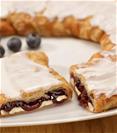Blueberry Cheesecake Kringle on a white plate surrounded by blueberries. 
