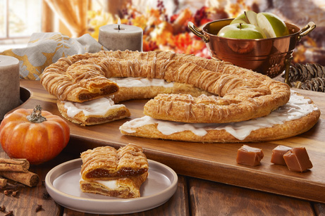 Pumpkin Caramel and Apple Cinnamon Kringle with slices cut out on separate plate surrounded by pumpkin, caramel cubes, apples and fall decorations. 
