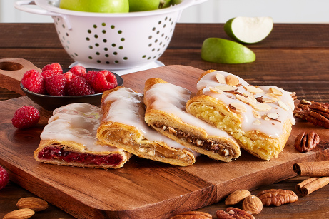 Slices of apple cinnamon, raspberry, pecan and almond Kringle on a white plate. 